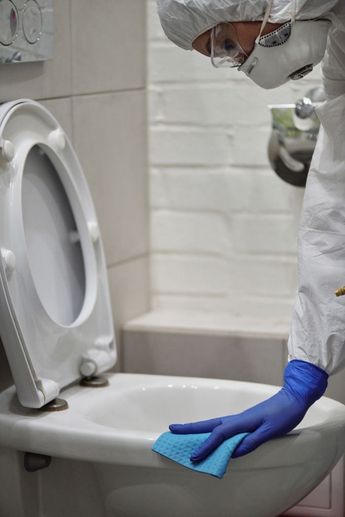 creative-01 Person in protective gear cleaning a toilet for sanitation and safety.