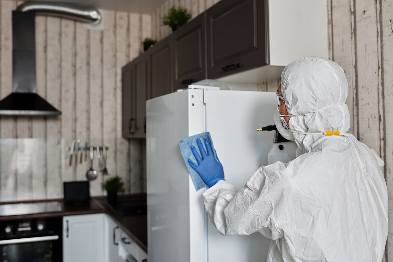 mobile-02 Individual in full protective gear cleaning kitchen fridge, promoting hygiene and safety.